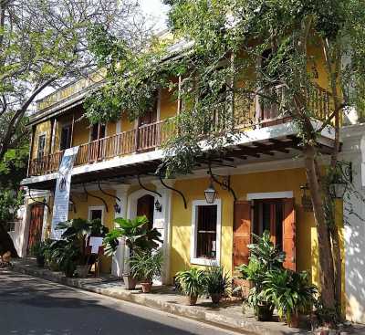 Maison coloniale jaune ornée de verdure et d'un balcon de bois