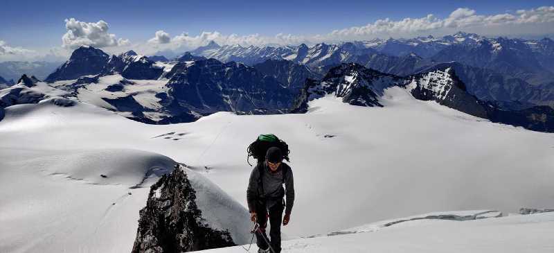 Un homme avec un gros sac à dos arrive au sommet d'une montagne enneigée