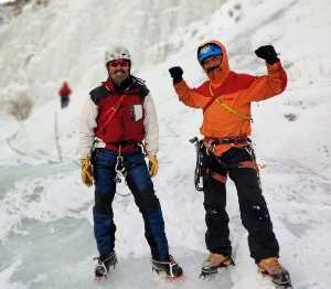 2 hommes aux pieds d'une paroi glacées font un signe de victoire