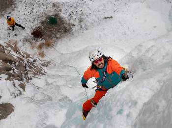 Un homme en orange et vert escalade une paroi glacée