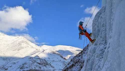 Un homme grimpe une cascade de glace avec à l'horizon des montagnes enneigées