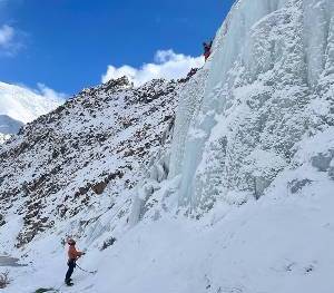 Un homme aux pieds d'une paroi de glace assure un autre qui grimpe