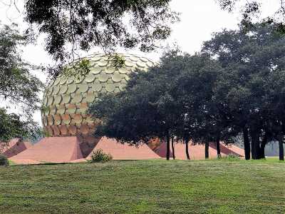 Immense boule dorée posée sur un socle de pierres roses, derrière des arbres