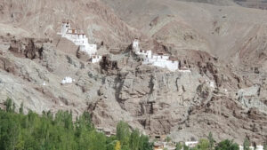 Des bâtiments blancs s'étagent sur une montagne comme accrochés à elle. Des arbres sont en bas de la photo